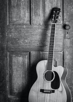 black and white photograph of an acoustic guitar in front of a door with wood paneling