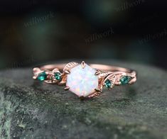 an opal and emerald ring sitting on top of a rock