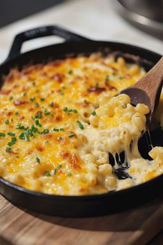 a skillet filled with macaroni and cheese on top of a wooden cutting board