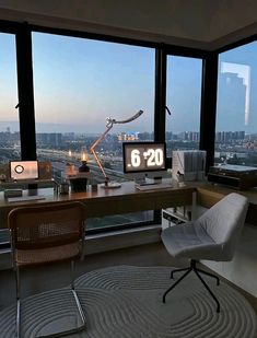 a desk with a computer on it in front of two large windows overlooking the city