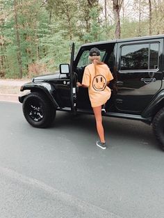 a woman standing next to a black jeep with a smiley face on it's hood