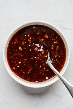 a white bowl filled with chili sauce on top of a marble counter next to a spoon