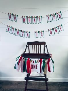 a wooden chair sitting in front of a white wall with christmas decorations hanging from it