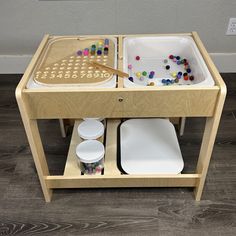 a child's wooden play table with two trays and bowls on the top