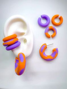 three pairs of purple and orange earrings on a white surface next to an earring