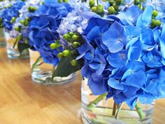 blue flowers are arranged in glass vases on a table