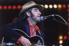 a man wearing a cowboy hat and holding a guitar in front of a microphone on stage