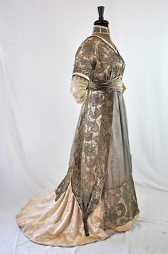 "EDWARDIAN AESTHETIC VELVET AND METALLIC LACE TRAINED GOWN, 1905 - 1910 One piece in construction, high net lace standing collar, V-shaped front and back with beadwork, metallic net lace over satin, velvet sash at waist adorned with metallic floral appliques. Double short sleeves with gold metallic lace netting, beaded dangles and ending with tiered valenciennes lace.  Streamer panels drapes its sides with metallic tassels. Nine fabric covered stays. Extensive hook and loop closures.  Chiffon inserts front and back. Satin and cotton lining. Unlabeled. APPROXIMATE MEASUREMENTS: Bust 37\" Waist 29\" Sleeve length 18\" Across back shoulder to shoulder 12\" Front shoulder to waist 17\" Front Shoulder to Hem line 53\" Back Shoulder to Hem line 61\". ERA: 1905 to 1910. CONDITION: In very good co Edwardian Aesthetic, Beaded Peacock, Fashion 1910, Augusta Auctions, Satin Evening Gown, 1910s Fashion, Peacock Dress, Edwardian Dress, Old Dresses