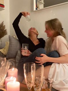 two women are sitting on the couch drinking wine and having fun with each other,