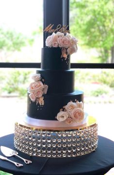 a three tiered black wedding cake with pink flowers on the top and gold trimmings