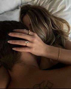 a woman is laying in bed with her hand on the back of her head and wearing a gold ring