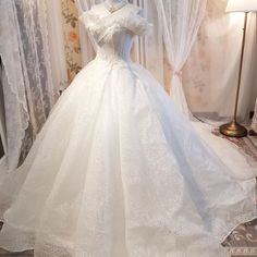 a white wedding dress on display in front of a window with curtains and drapes