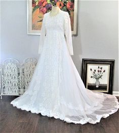 a white wedding dress is on display in front of a floral painting and framed artwork