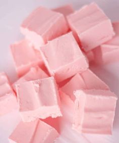 some pink marshmallows are on a white plate and have been cut into squares