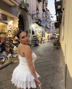 a woman in a white dress is standing on the side walk with her hand under her hip