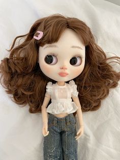 a doll with long brown hair laying on a white sheet