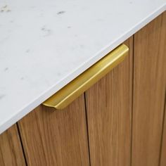 a white counter top sitting next to a wooden cabinet with gold handles on it's sides