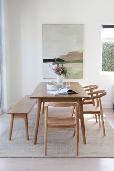 a dining room table with four chairs and a vase on the table next to it