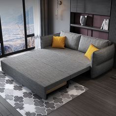 a grey couch with yellow pillows in front of a large window and book shelf on the wall