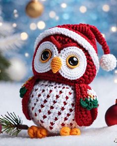 a crocheted owl sitting on top of a snow covered ground next to a christmas tree