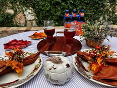 the table is set with plates, cups and vases filled with autumn leaves on it