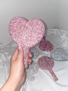 a hand holding a pink heart shaped bag with glitters on it and five other hearts in the background