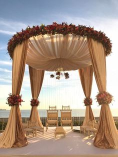 an outdoor wedding setup with chairs and flowers on the canopy over looking the ocean at sunset