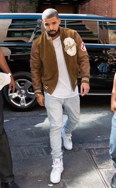 a man in white shirt and brown jacket walking down the street with his hand on his hip