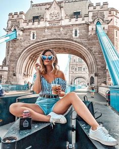 a woman sitting on the edge of a bridge while holding a drink and looking at her cell phone