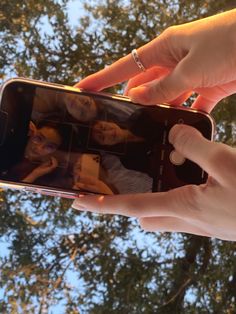 someone taking a photo with their cell phone in front of some trees and blue sky