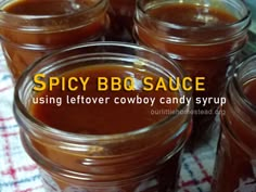 several jars filled with hot sauce sitting on top of a checkered table cloth and text spicy bbq sauce using leftover cowboy candy syrup