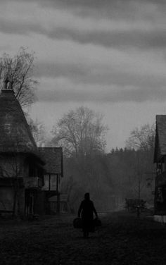 black and white photograph of person walking in front of old houses