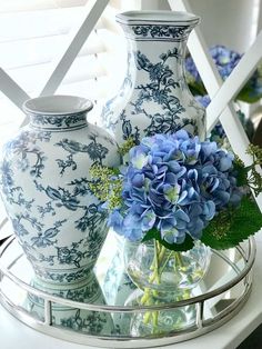 three blue and white vases with flowers in them on a glass tray next to a mirror