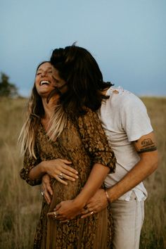 a man and woman hugging each other in the middle of a field with tall grass