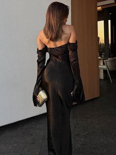 a woman in a black dress is walking down the street with her back to the camera