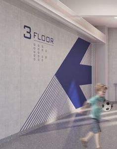 a young child is playing with a soccer ball in the room that has a floor sign on it