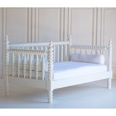 a small white bed with wooden posts and pillows on top of the headboard, in front of a wall