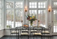 a dining room table with four chairs in front of it and windows on the wall