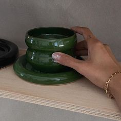 a person's hand holding a green coffee cup on top of a wooden shelf