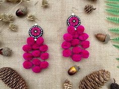 two pairs of pink pom - pom earrings sitting next to pine cones and acorns