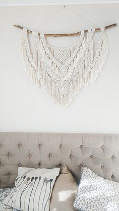 a bed with white pillows and a macrame wall hanging above the headboard