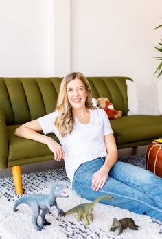 a woman sitting on the floor next to some toy dinosaurs and a couch in front of her