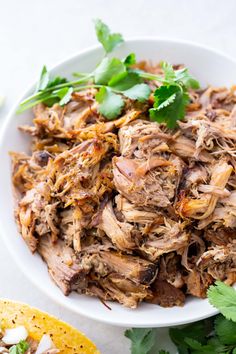 shredded pork with cilantro on a white plate next to tortilla chips