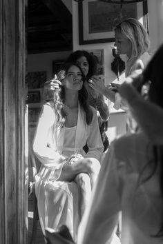 two women in robes are getting their hair done by a woman who is looking at her phone