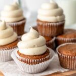 cupcakes with white frosting sitting on top of a wooden cutting board