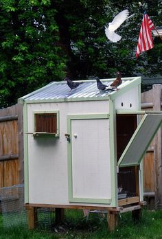 a chicken coop with two birds on the roof and an american flag flying above it