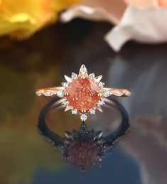 an orange diamond ring sitting on top of a black surface with flowers in the background