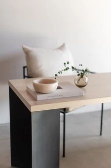 a table with a book, bowl and vase sitting on it next to a couch