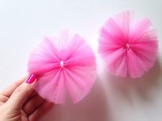 two pink tulle flowers are being held by a woman's hand on a white surface