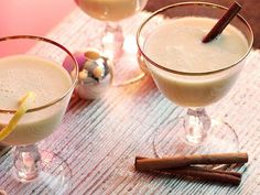 two glasses filled with drinks sitting on top of a table next to cinnamon sticks and an orange slice